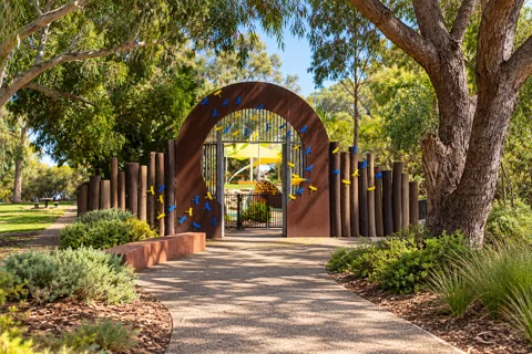 Rust-brown entrance arch, blue and yellow dragonflies and timber posts at Bibra Lake Regional Playground
