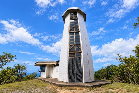 Fitzroy Island lighthouse with a tall white tiled facade, central windows and a closed mesh gate.