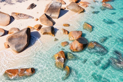 Large weathered granite boulders in pale coral sand and clear water at Nudey Beach on Fitzroy Island.