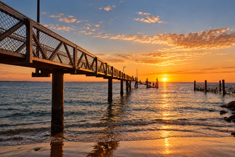 The metal-railed Amity Point jetty extending over Moreton Bay at sunset.