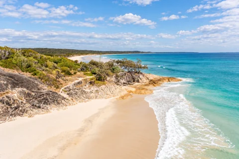 Pale sand and a low rocky point beside the turquoise water at Cylinder Beach.